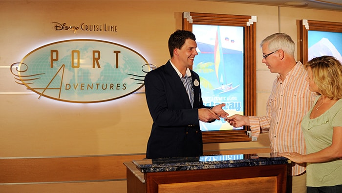 Un hombre asiste a los Huéspedes con sus planes, frente al logotipo de Port Adventures de Disney Cruise Line 
