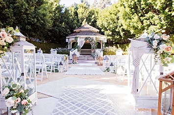An outdoor area set up for a wedding with chairs on either side of an aisle and a gazebo decorated with flowers at the end of the aisle