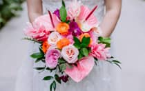 A bride’s hands holding a vibrant bouquet of flowers including roses, orchids and lilies