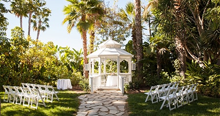 Two sections of a chairs face a gazebo in a garden with palm trees and lush vegetation