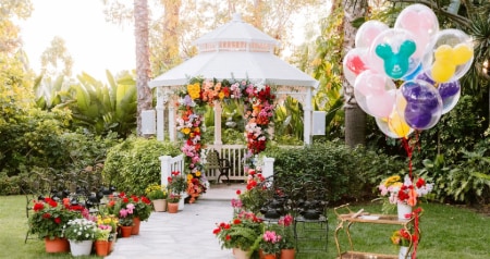 Two sections of a chairs face a gazebo in a garden with palm trees and lush vegetation