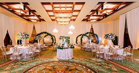 A ballroom with set tables, floral arrangements and arches