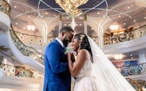 A bride and a groom stand close and hold hands in the romantic lighting of a Disney cruise ship atrium