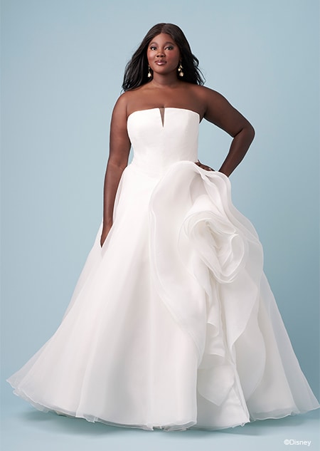 A bride wearing a strapless Belle inspired A line wedding gown featuring an illusion neckline and a layered skirt gathered at the hip