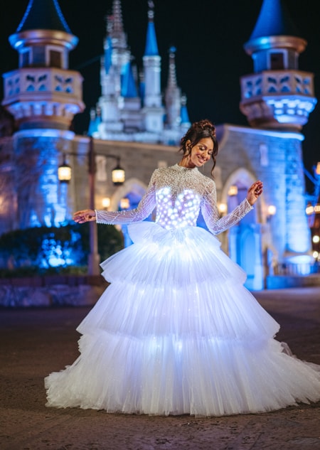 A bride in an illuminated wedding gown standing next to a castle at Walt Disney World Resort