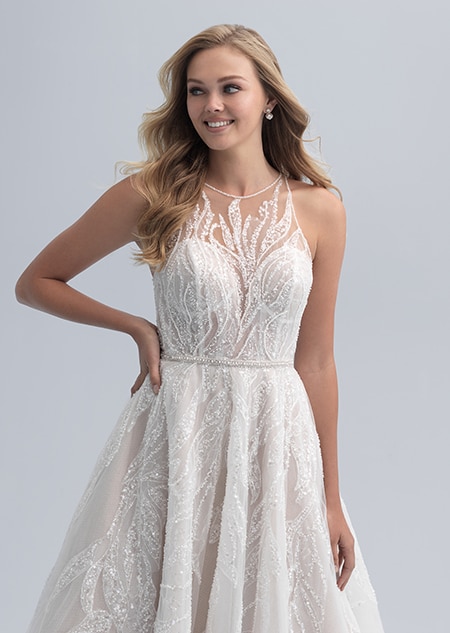 A bride poses with her hand resting on her hip while wearing a wedding dress with an illusion neckline