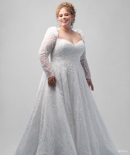 The front of a bride wearing a Cinderella inspired A line gown featuring a V neckline, beading and long, sheer sleeves