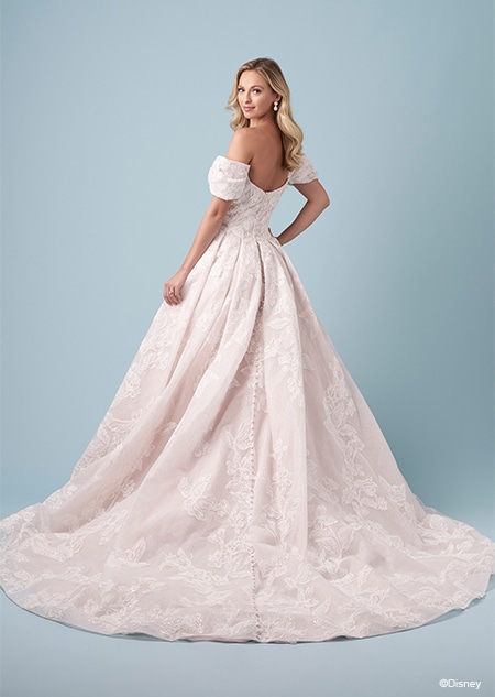 A bride wearing an Aurora inspired A line wedding gown featuring embroidery and off the shoulder sleeves