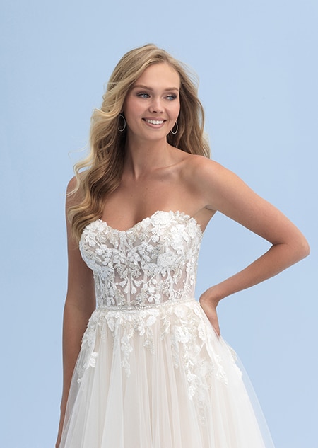 A bride poses with her hand on her hip while wearing an off the shoulder wedding dress
