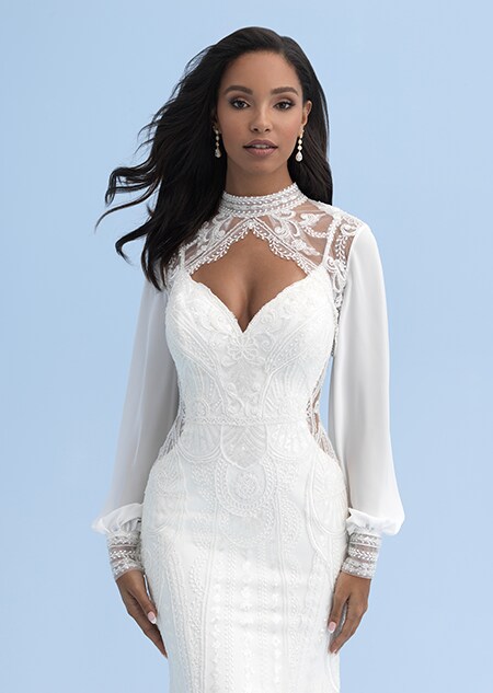 A bride in a form fitting wedding dress with cutouts on the sides and an overlay with long sleeves and lace above the neckline