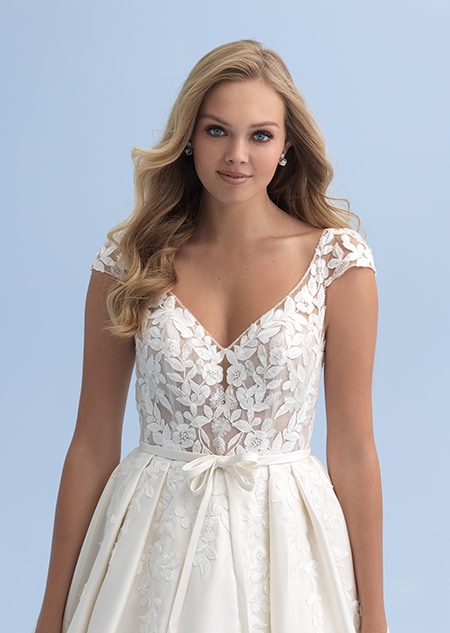 A close up of a woman in a wedding dress with cap sleeves and a partially see thru bodice with a belted waist A close up of a woman in a wedding dress with cap sleeves and a partially see thru bodice with a belted waist