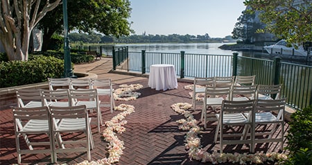 An outdoor ceremony setup with classic wedding chairs, flower petals lining the aisle and a waterfront view