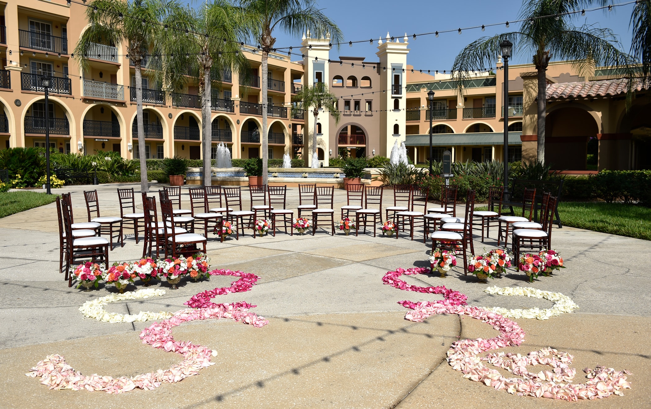 Rose petals lead to a group of chairs arranged in a semi-circle on a courtyard with a large water fountain
