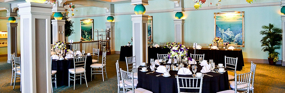 An indoor venue with framed pictures of ocean inspired art, chairs and tables topped with floral centerpieces, plates, glasses and napkins