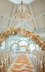 Disney's Wedding Pavilion featuring pews, a vaulted ceiling, a chandelier, floral arches and flower petals strewn down the aisle