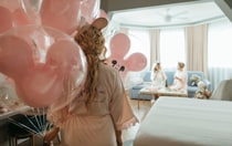 A woman holding Mickey Mouse balloons in a hotel suite wearing a robe with the word, 'Bridesmaid'