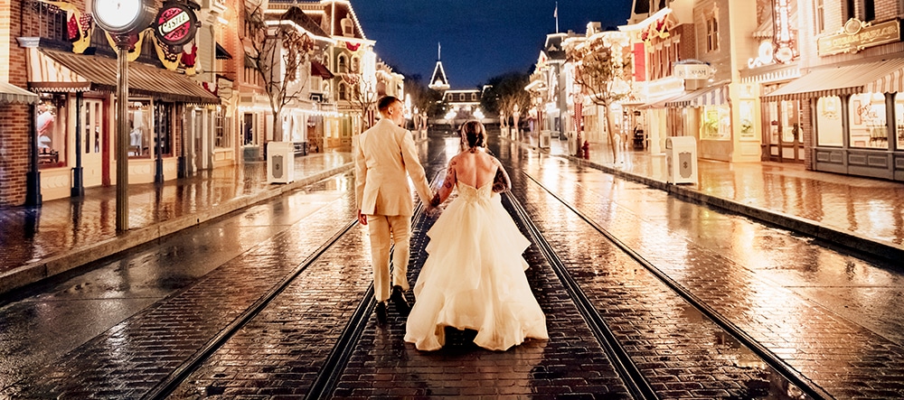 A bride and a groom walk down an empty Main Street, U S A in Magic Kingdom park at Walt Disney World Resort lit up at night