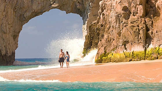 A couple holds hands while walking on the beach by El Arco in Cabo San Lucas, Mexico