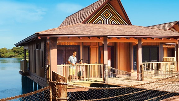 A father and son wearing Mickey Ears on the porch of a Polynesian-themed, overwater Bungalow