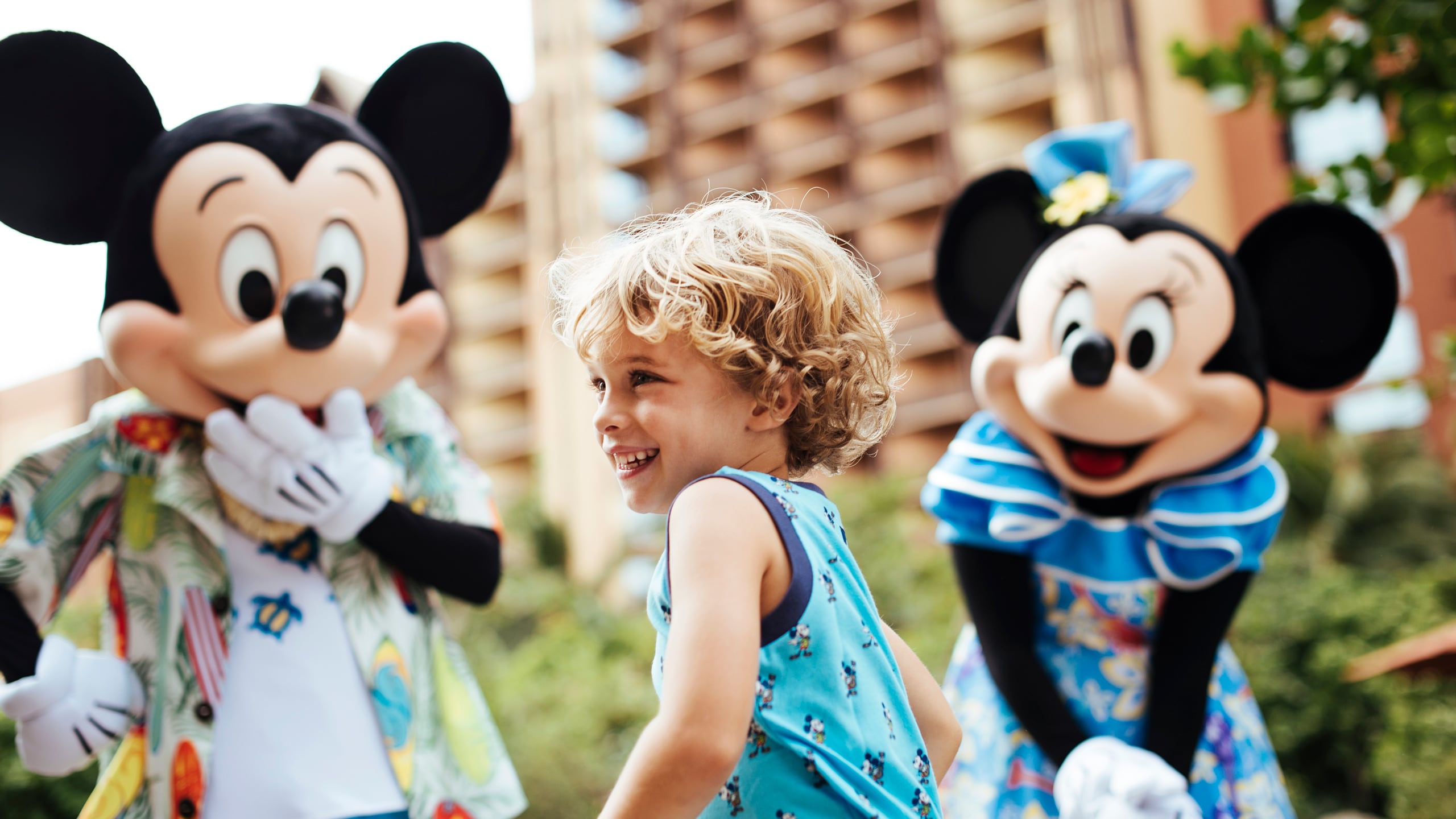 A young child smiling while standing near Mickey Mouse and Minnie Mouse