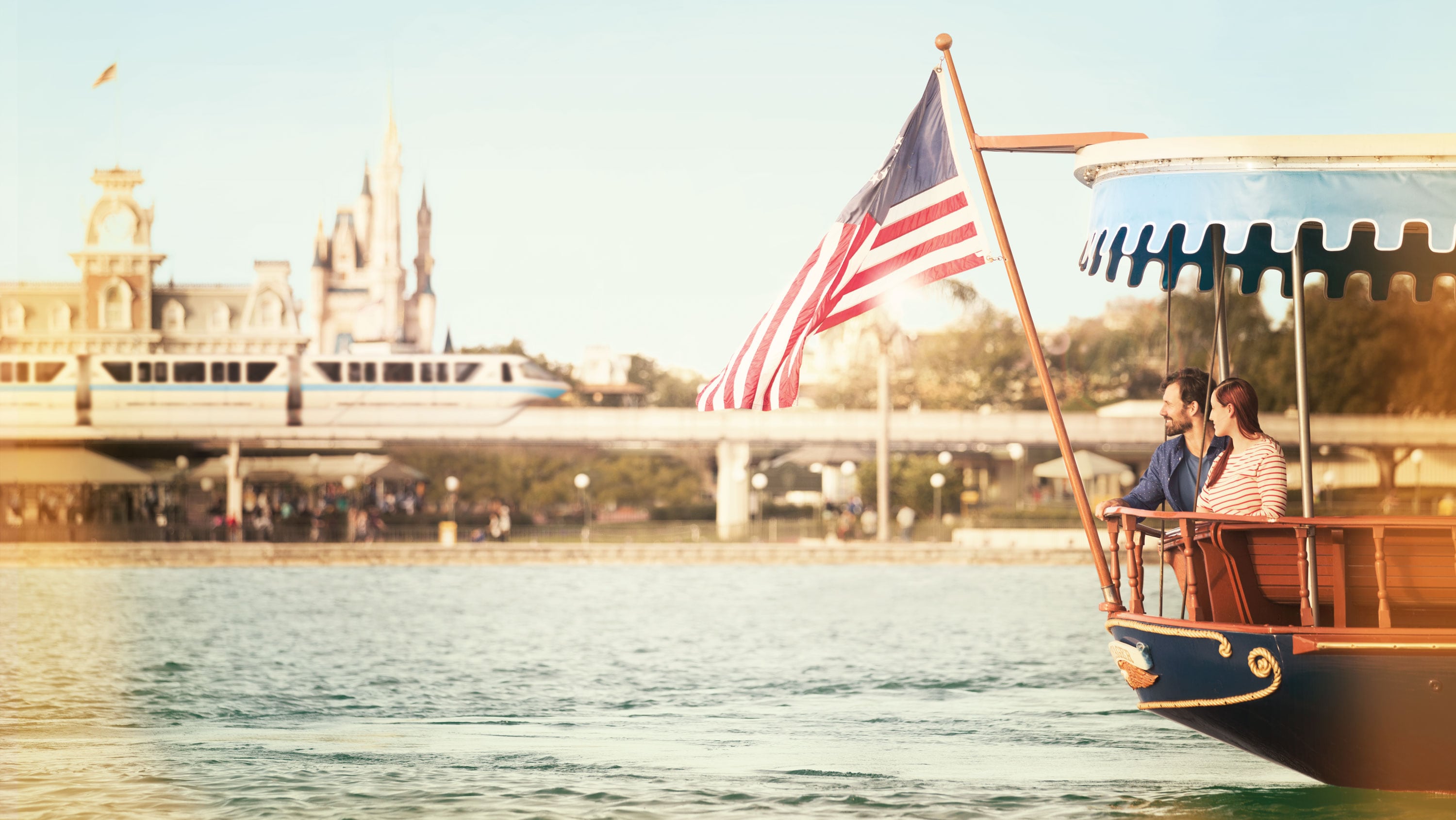 A couple glides past Magic Kingdom park aboard an American flag bearing ferryboat.