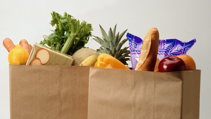 Two packed bags of groceries, with apples, celery, a baguette and other food showing