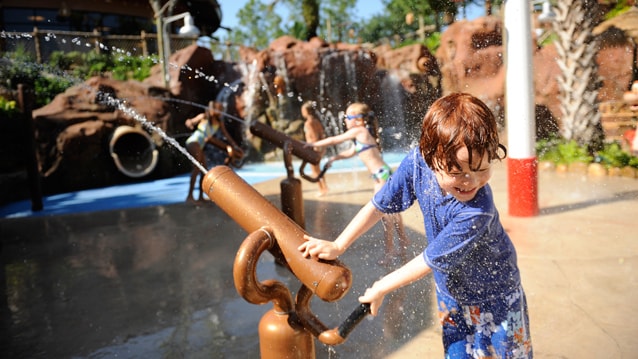 Kids stand outside a swimming pool playing with squirting cannons