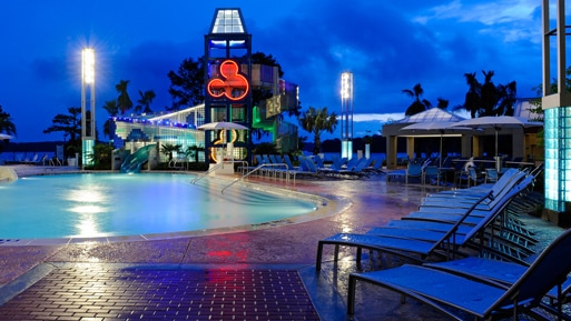 A pool area with waterslide, lounge chairs and umbrellas, illuminated at night