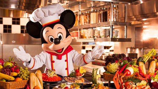 Mickey Mouse dressed in chef attire and surrounded by food at Chef Mickey restaurant