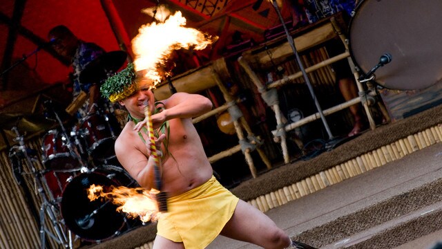 A male fire dancer wearing a loincloth and headpiece, performing a Polynesian dance