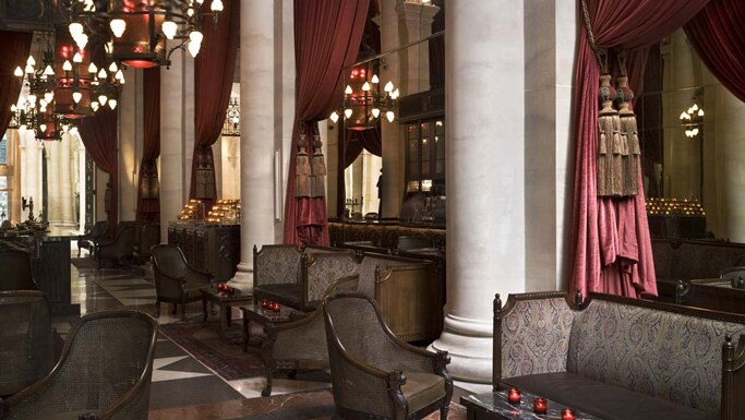 A lounge with chandeliers, red tapestries and marble columns