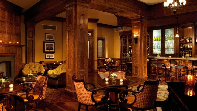 A bar and lounge with wood tables, chairs and columns at The Sagamore Resort