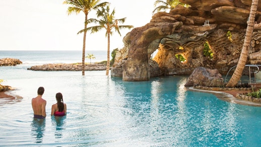 A man and woman standing in an infinity pool at Aulani, A Disney Resort & Spa