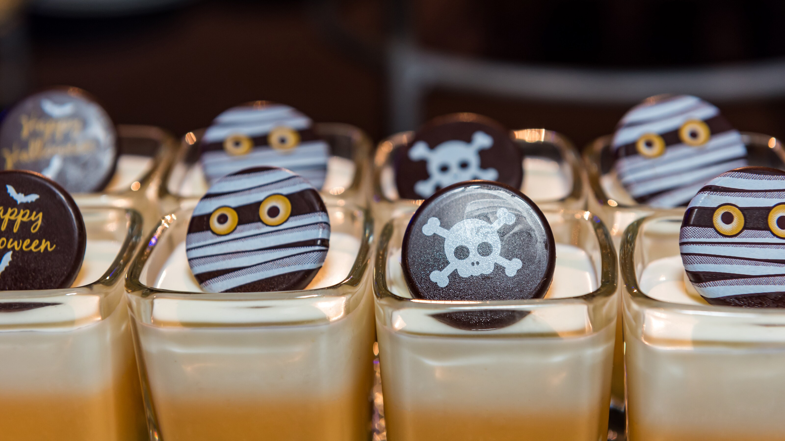 Several mini desserts served in small glasses, topped with Halloween themed chocolates