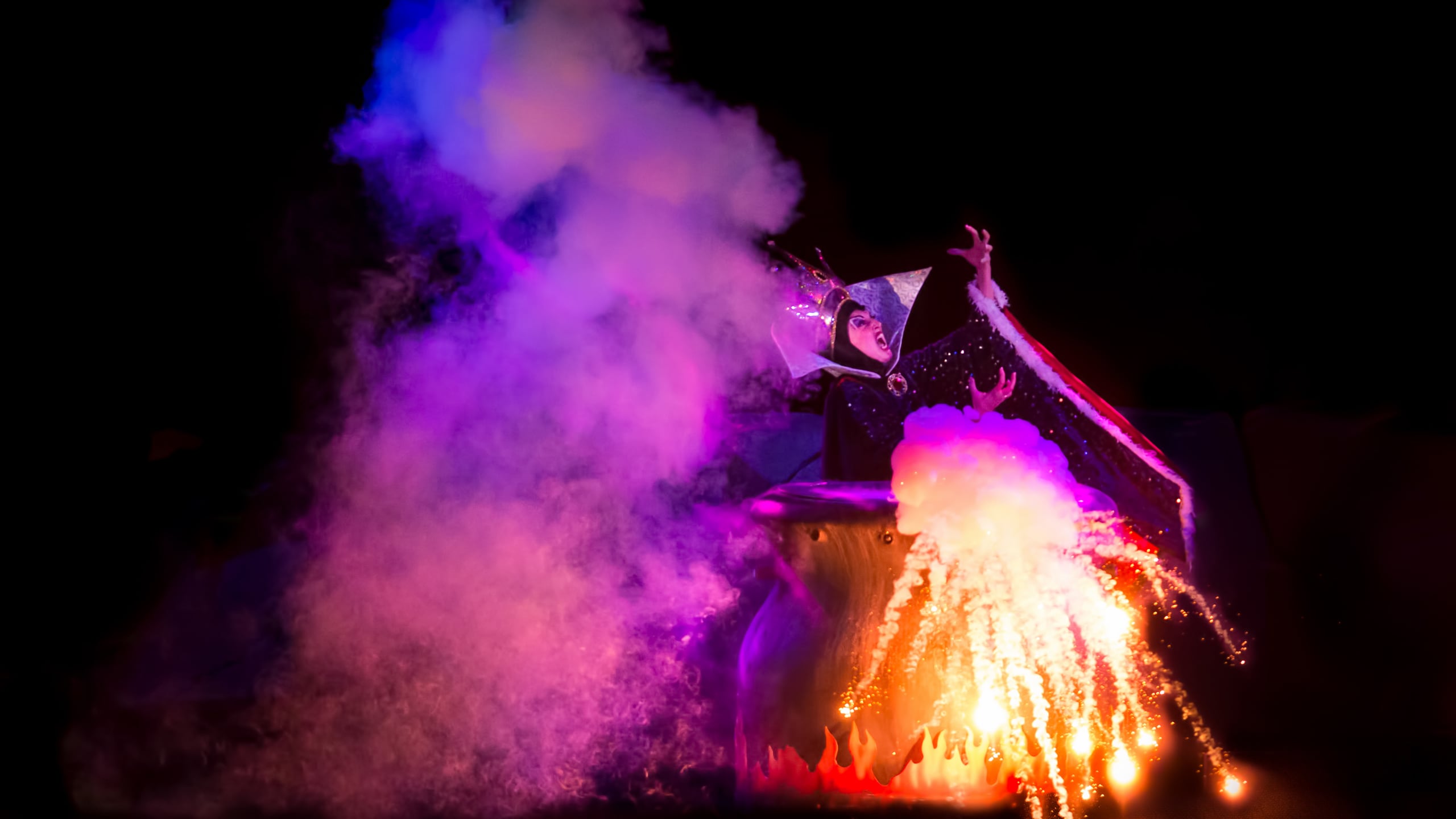 Maleficent stands beside a smoking cauldron