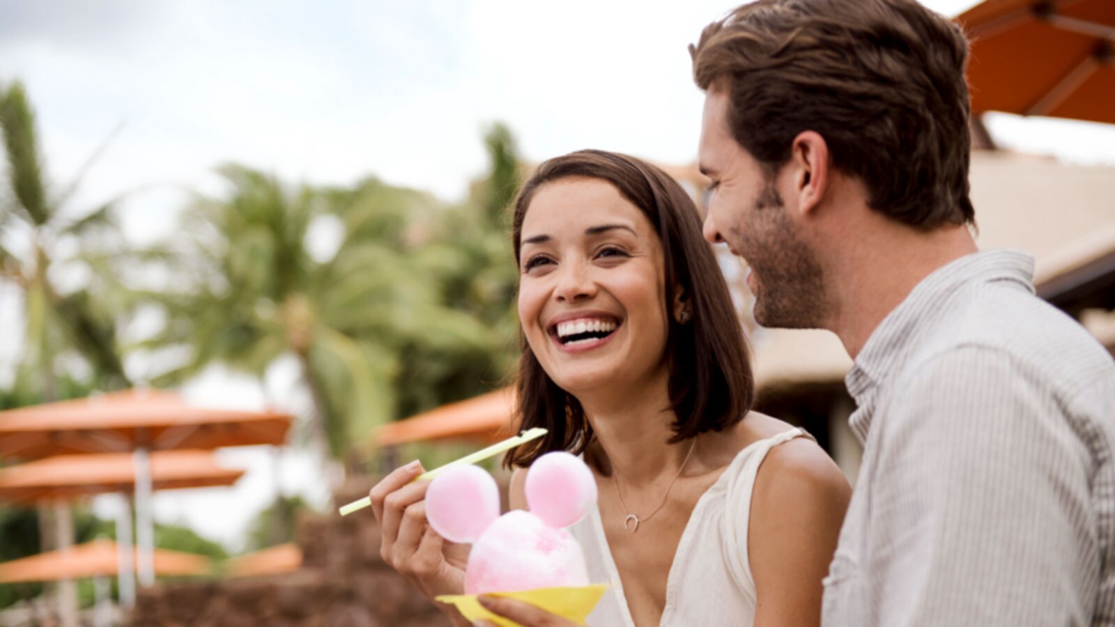 A man smiles as he watches a woman holding a Mickey Mouse shaped shave ice and a straw