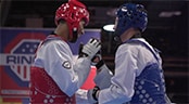 Two men wearing martial arts uniforms, including helmets and body pads, shake hands