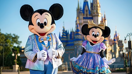 Mickey and Minnie strike a pose in fancy clothing in front of Cinderella Castle