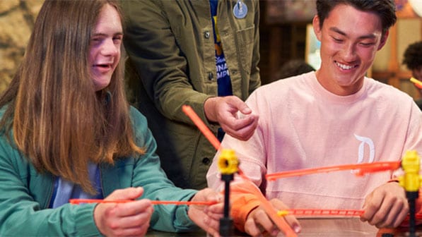 Disney Imagination Campus students sit around a table as they build a small scale roller coaster