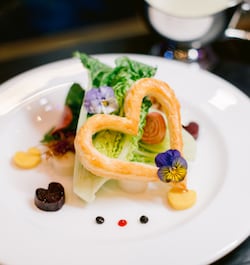 An elegantly plated salad course with a heart shaped pastry and edible flowers